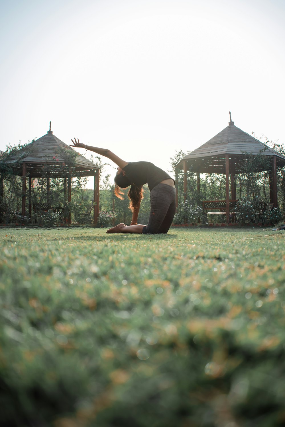 Frau in schwarzem Tanktop und schwarzer Hose beim Yoga auf grünem Rasen tagsüber