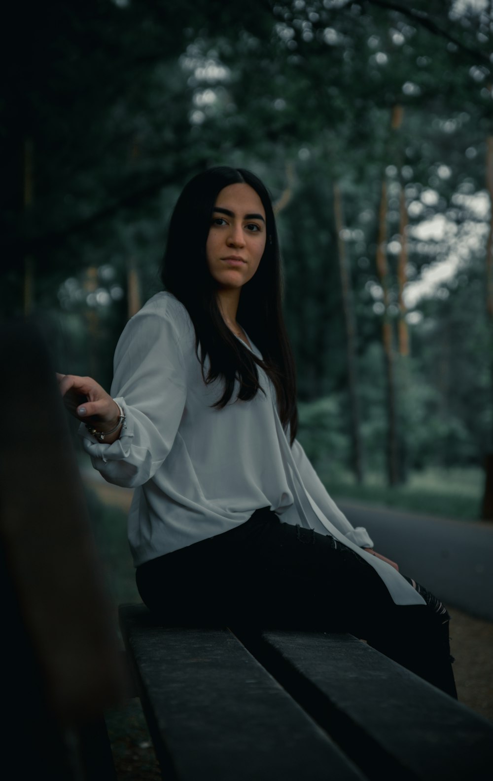 woman in white long sleeve shirt and black skirt sitting on brown wooden bench during daytime