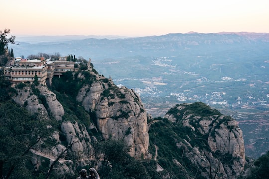 white concrete building on top of brown rocky mountain in Santa Maria de Montserrat Abbey Spain