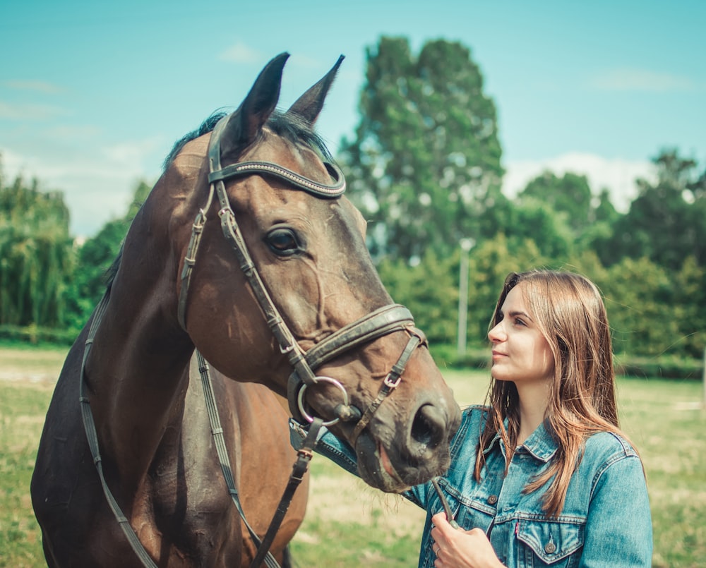 girl in blue denim jacket standing beside brown horse during daytime