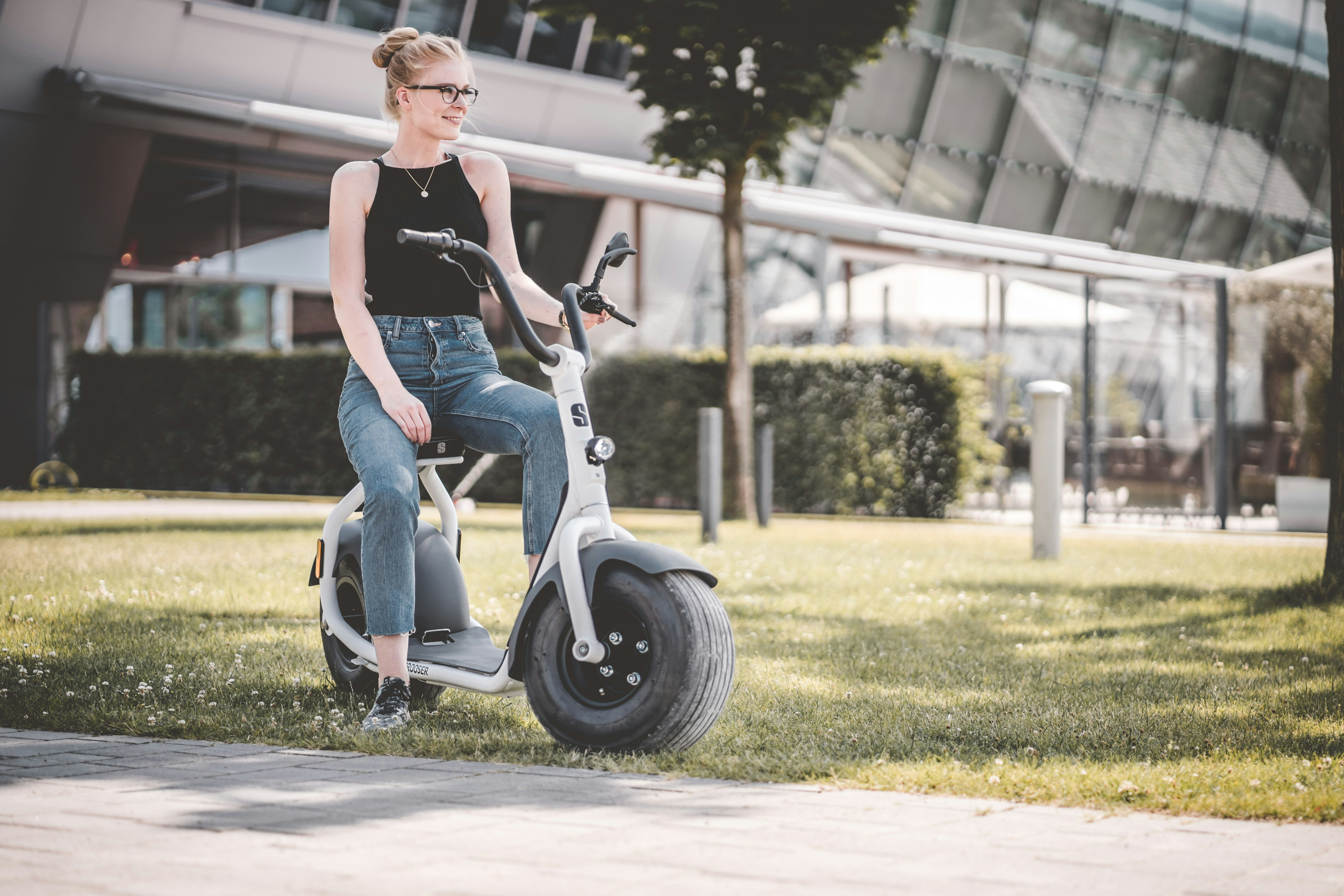 woman in black tank top and blue denim shorts riding white motor scooter during daytime