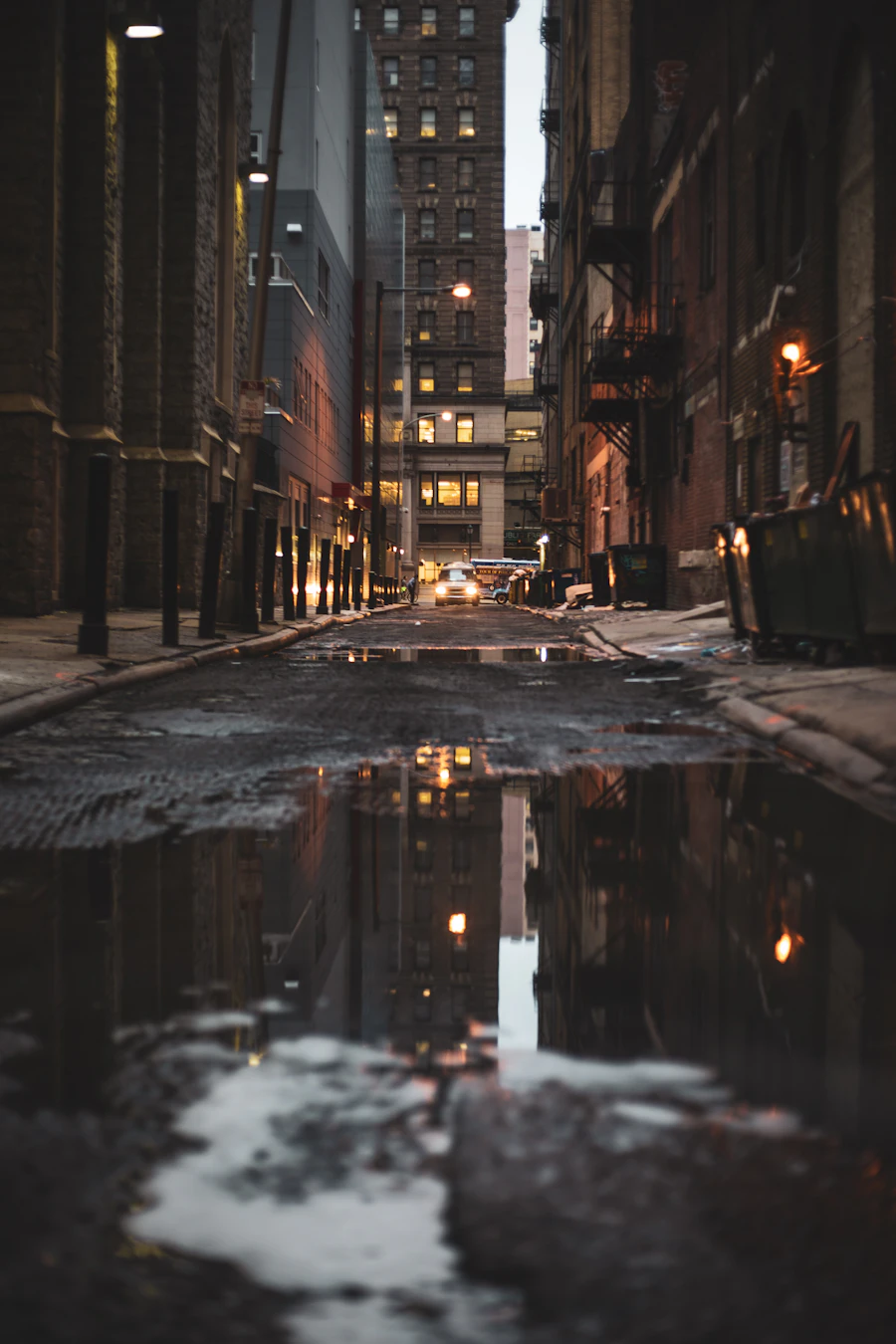 A narrow street with puddles reflecting lamps