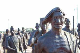 A group of bronze statues with a prominent figure in glasses and traditional attire standing in front. The statues appear to represent historical figures engaged in a march or procession.