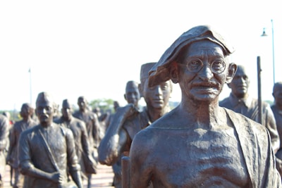 A group of bronze statues with a prominent figure in glasses and traditional attire standing in front. The statues appear to represent historical figures engaged in a march or procession.