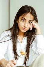 woman in white long sleeve shirt holding yellow flower