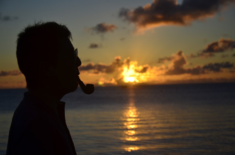 silhouette of woman standing near body of water during sunset