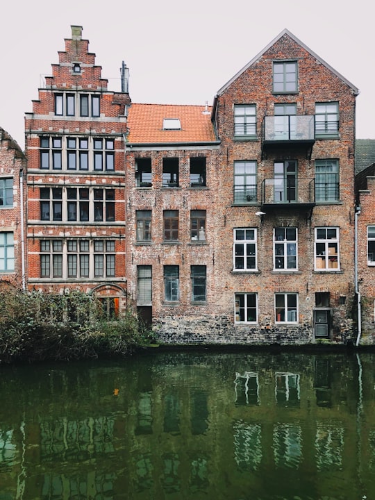 brown concrete building beside river during daytime in Ghent Belgium
