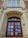 A grand, old architectural building entrance featuring a large wooden door with multiple panels and ornate stone carvings around the arch. Above the door are decorative windows with diamond-shaped glass panes, and the words 'Arts Building' etched into the stone. The structure is made of a combination of brick and stone, showcasing intricate detailing and craftsmanship.
