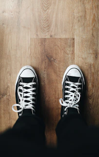 Close-up of classic white All Star sneakers on a wooden floor with soft natural light.
