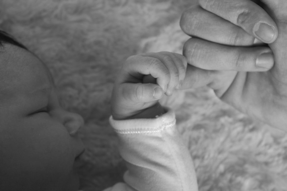 사람의 손을 잡고 있는 아기의 회색조 사진