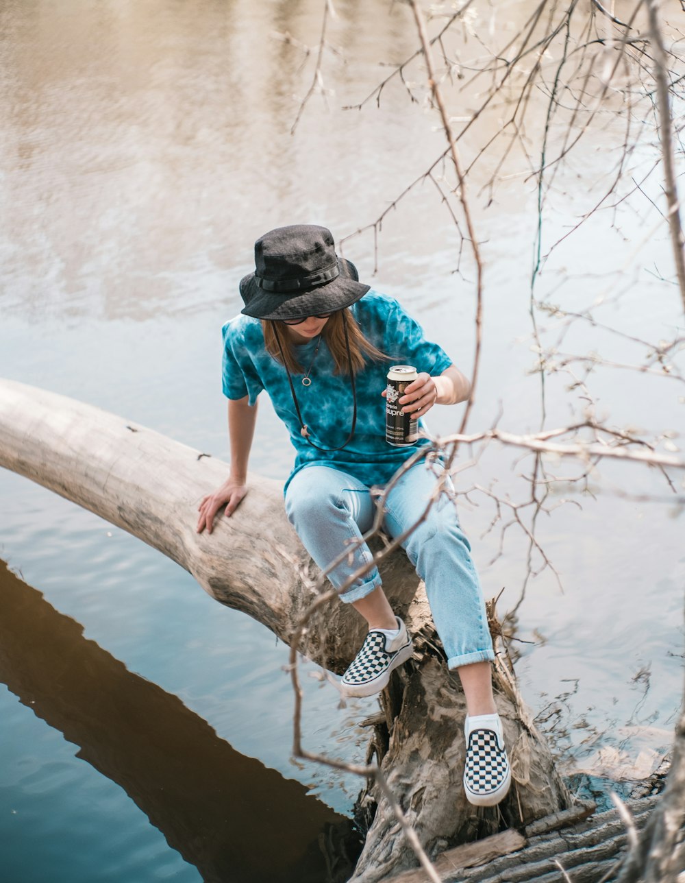 Femme en chemise bleue et pantalon blanc et noir assise sur un tronc d’arbre brun pendant la journée