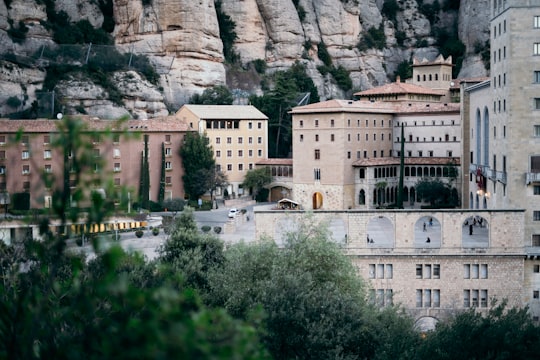 white concrete building near green trees and mountain during daytime in Santa Maria de Montserrat Abbey Spain