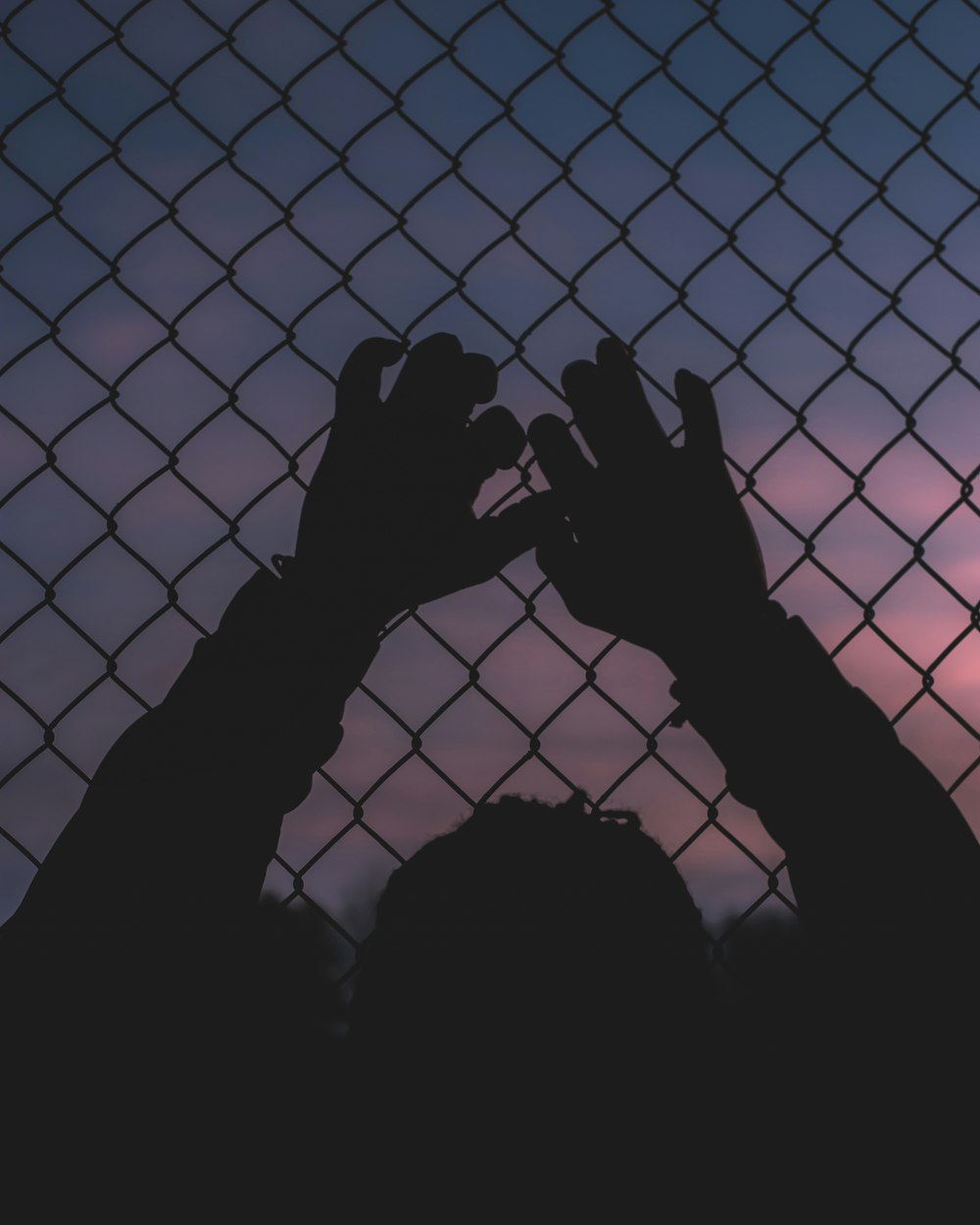 silhouette of persons hand on chain link fence