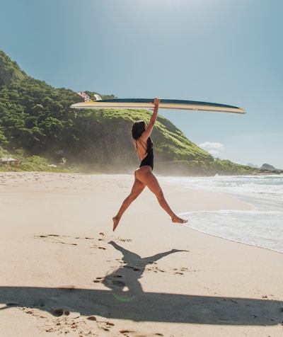 woman in black bikini holding white surfboard on beach during daytime