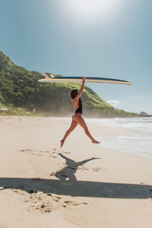 A sunlit beach scene in California with a teenage girl laughing and holding a surfboard.