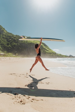 A sunlit beach scene in California with a teenage girl laughing and holding a surfboard.