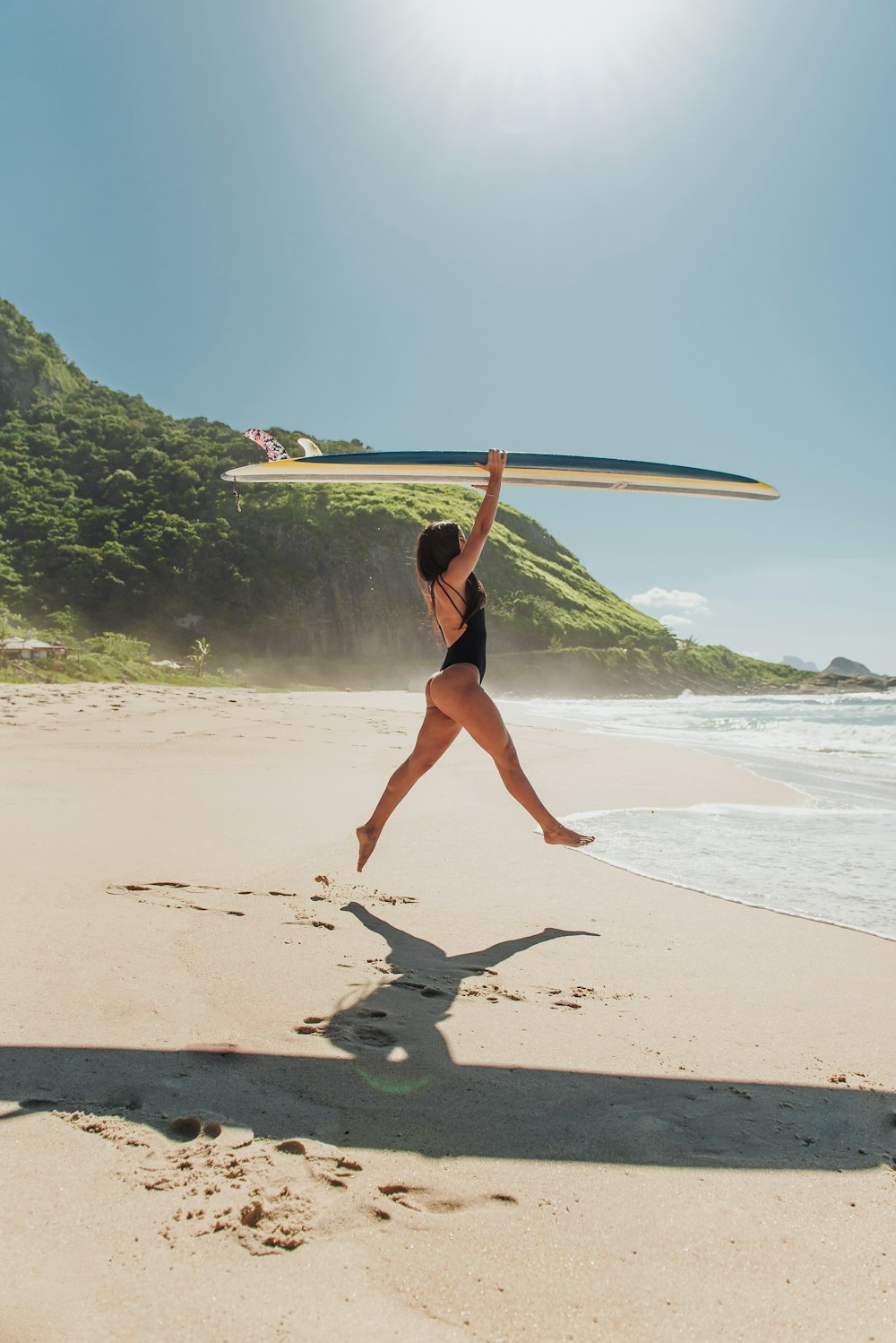 Frau im schwarzen Bikini mit weißem Surfbrett am Strand tagsüber