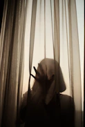 A silhouette of a figure behind sheer curtains, creating an air of mystery.