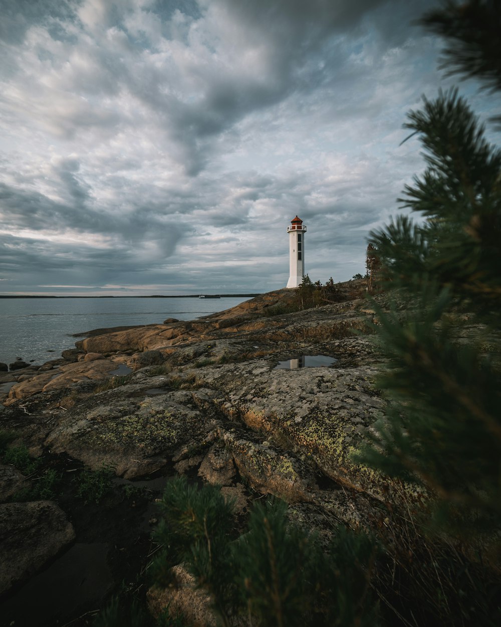white and brown lighthouse on brown rock formation near body of water under white clouds during