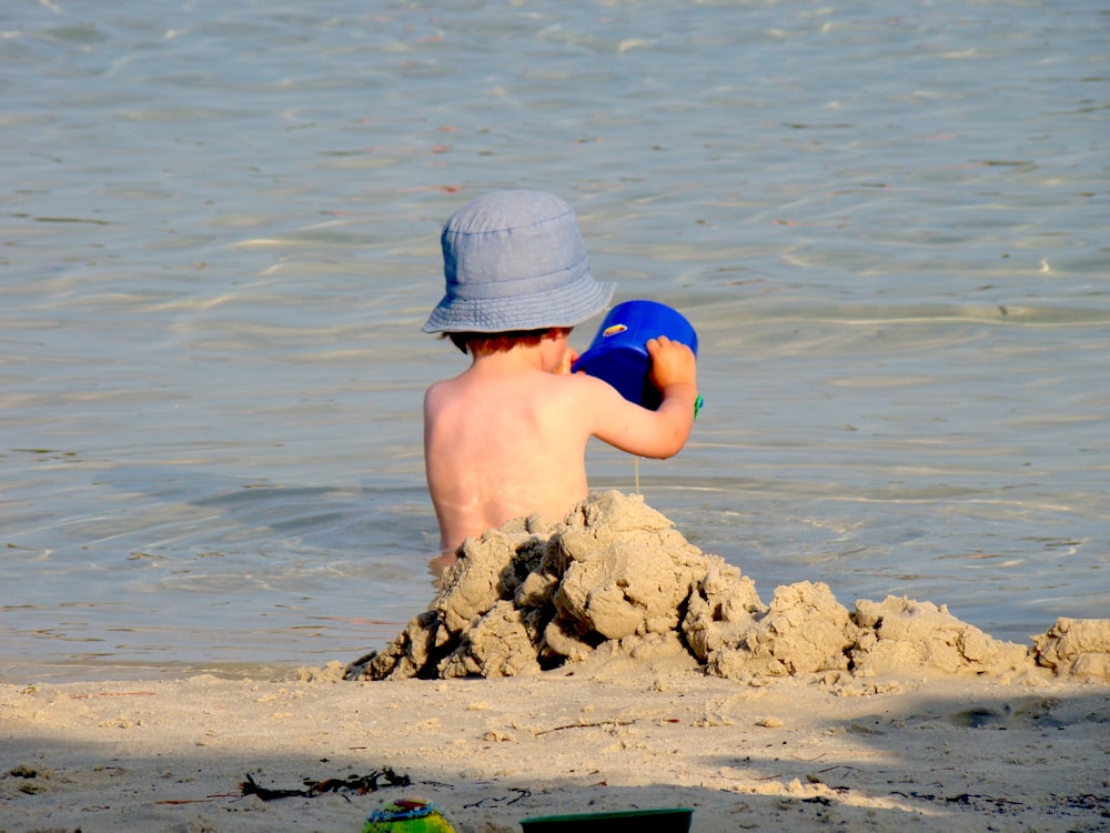 Junge in blauen Shorts sitzt tagsüber auf braunem Felsen im Meer