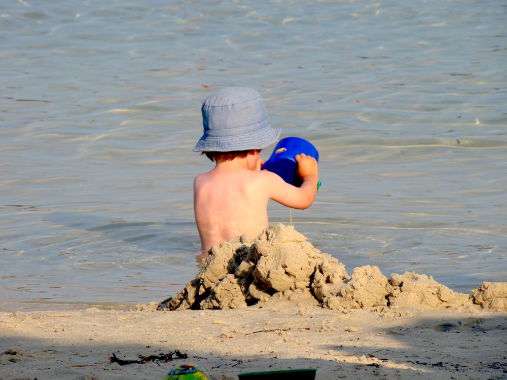 Chico en pantalones cortos azules sentado en la roca marrón en el mar durante el día