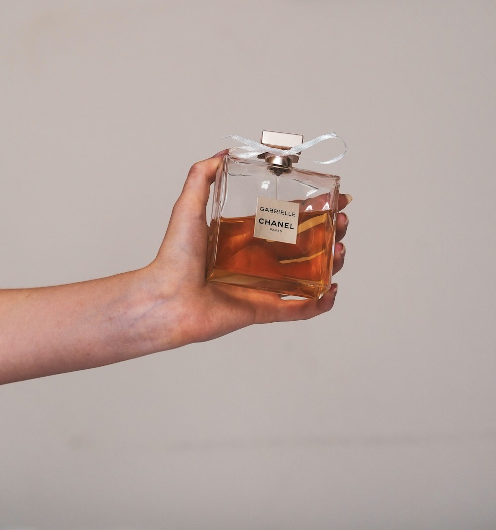 Persona sosteniendo un frasco de perfume de vidrio transparente