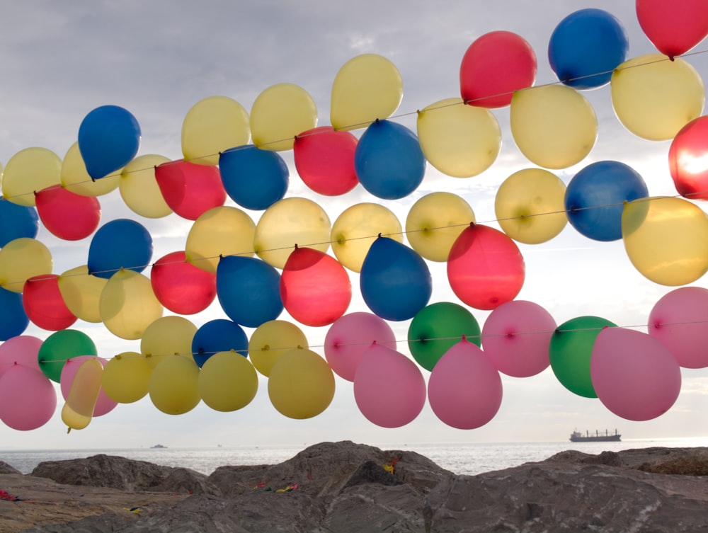 multi colored balloons on brown rock formation near body of water during daytime