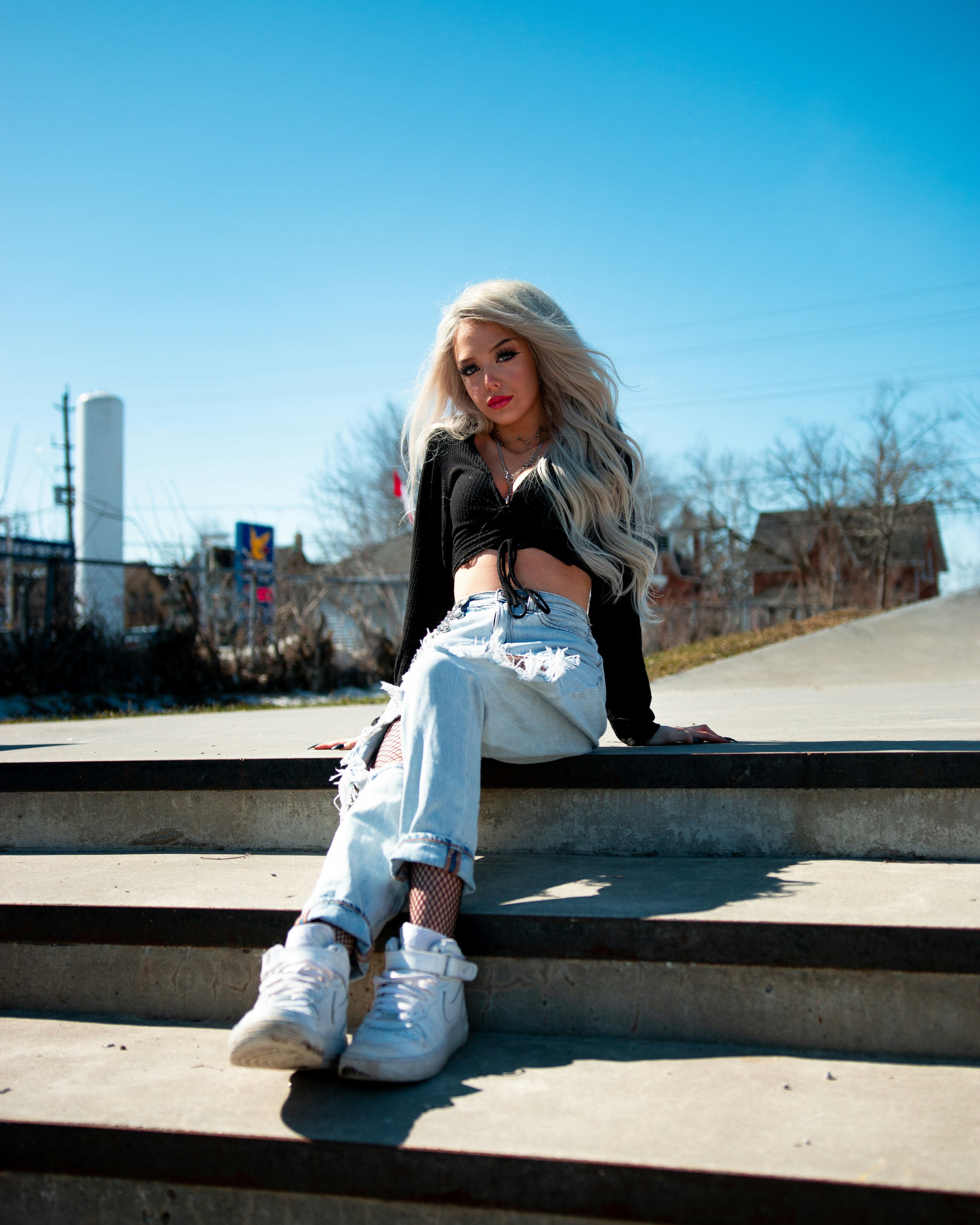 woman in black jacket and blue denim jeans sitting on brown wooden bench during daytime