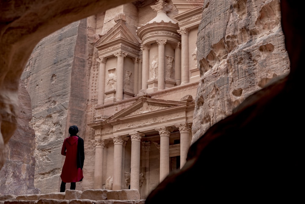 Femme en manteau rouge debout devant un bâtiment en béton blanc pendant la journée