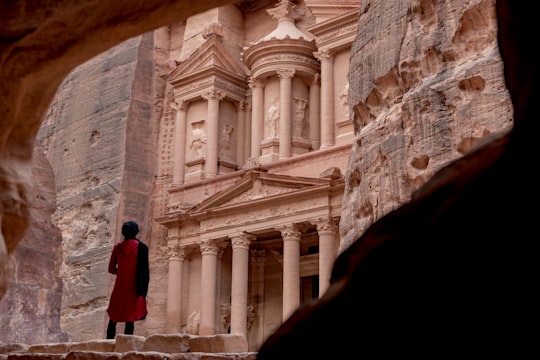 woman in red coat standing in front of white concrete building during daytime in Petra Jordan