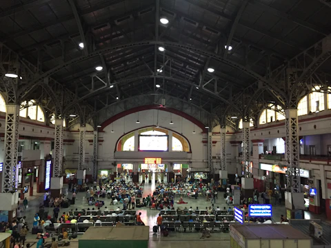 A panoramic view of a bustling Delhi railway station adorned with large LED advertising screens.