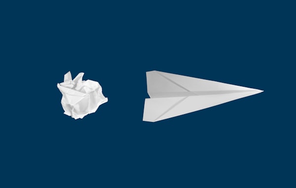 a crumpled piece of paper and a paper airplane, as if the former was smoothed out into the latter