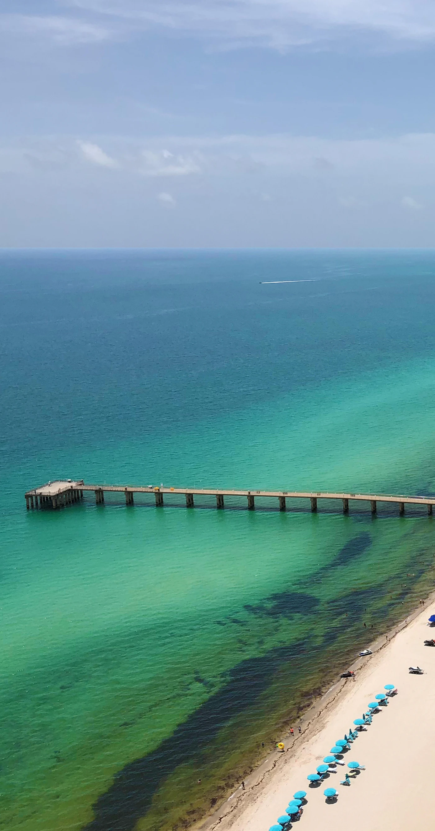 A fishing pier reaching out over clear green water off a northeast Miami-Dade beach.