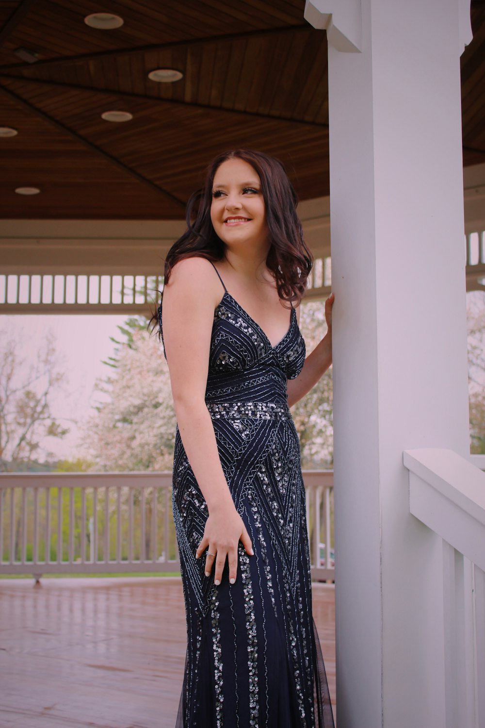 woman in blue and white floral spaghetti strap dress standing beside white wooden fence during daytime