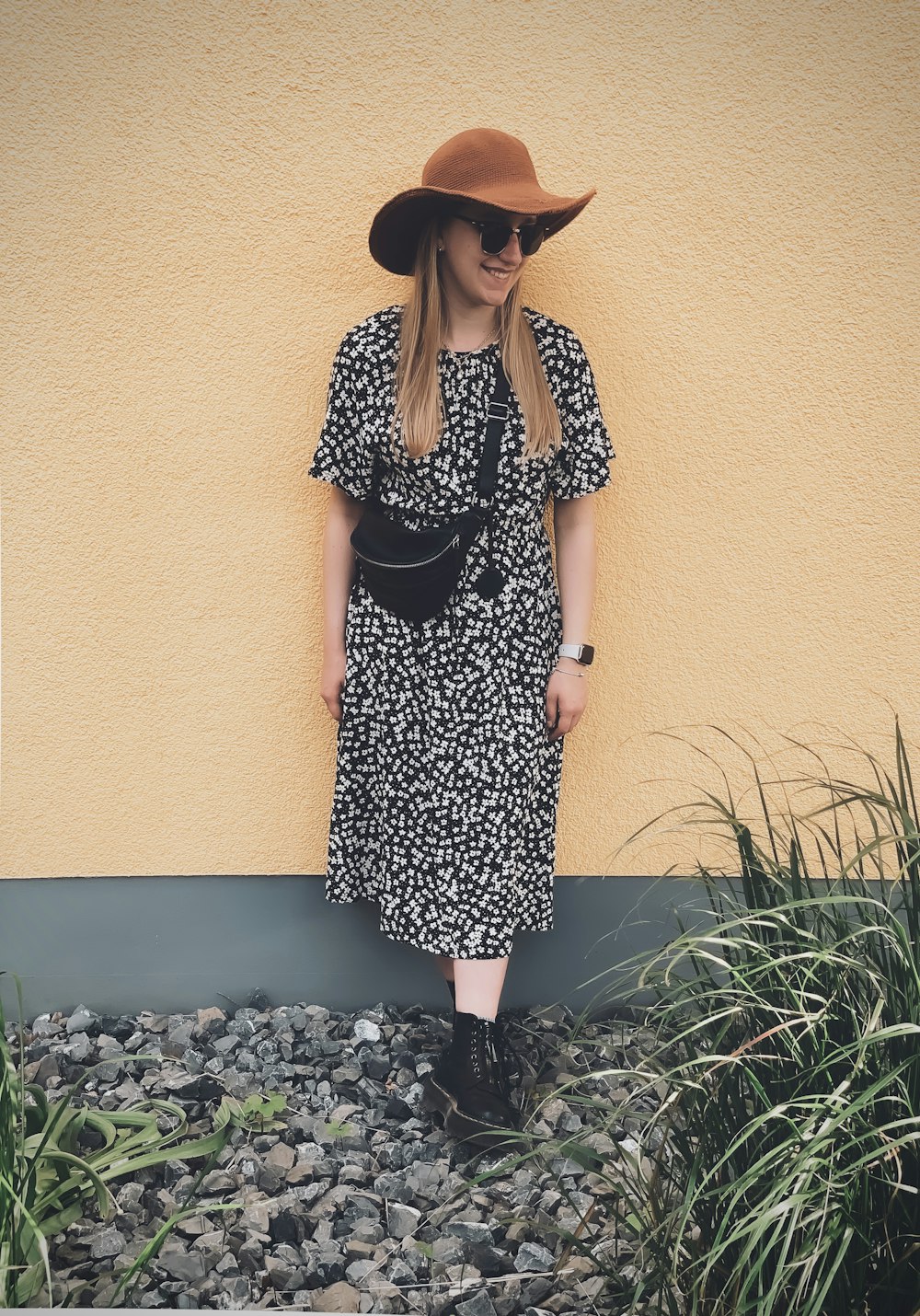 woman in black and white polka dot dress wearing brown sun hat standing beside green plants