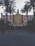A retro-styled theater with a prominent Hollywood sign is flanked by tall palm trees. The facade features art deco architectural elements and a notable marquee displaying movie showtimes. Street lamps with orb lights line the entrance, creating a classic cinematic atmosphere.