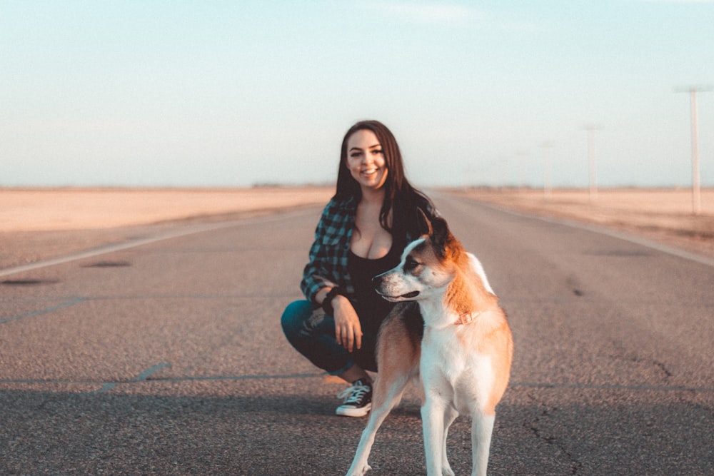 a woman kneeling down next to a dog on a road