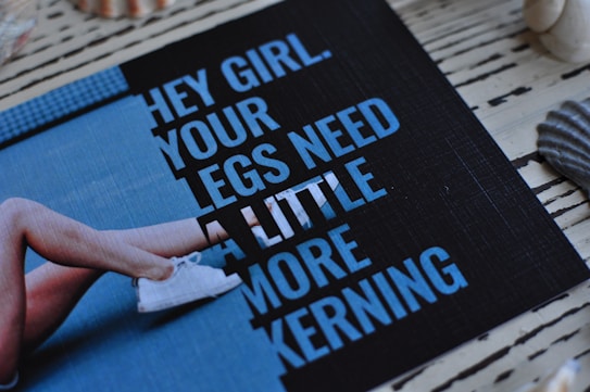 A printed card with a humorous text passage is placed on a striped wooden surface, surrounded by seashells and featuring an image of crossed legs in sneakers. The text humorously comments on typography spacing.