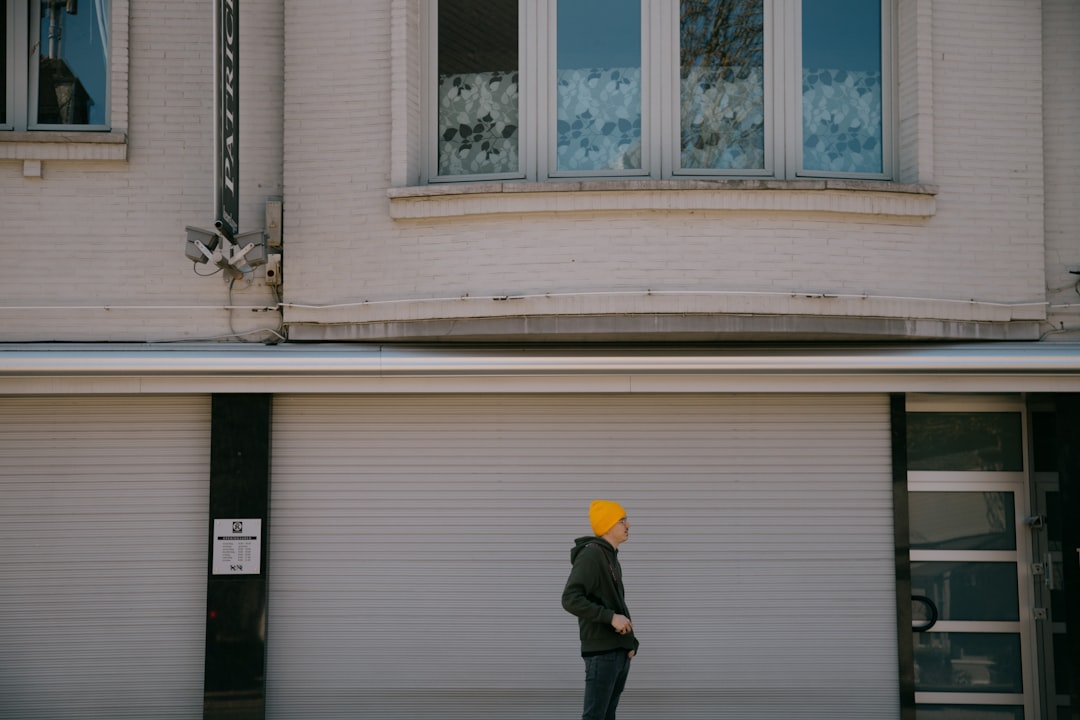 man in black jacket and black pants standing near white wooden framed glass window during daytime