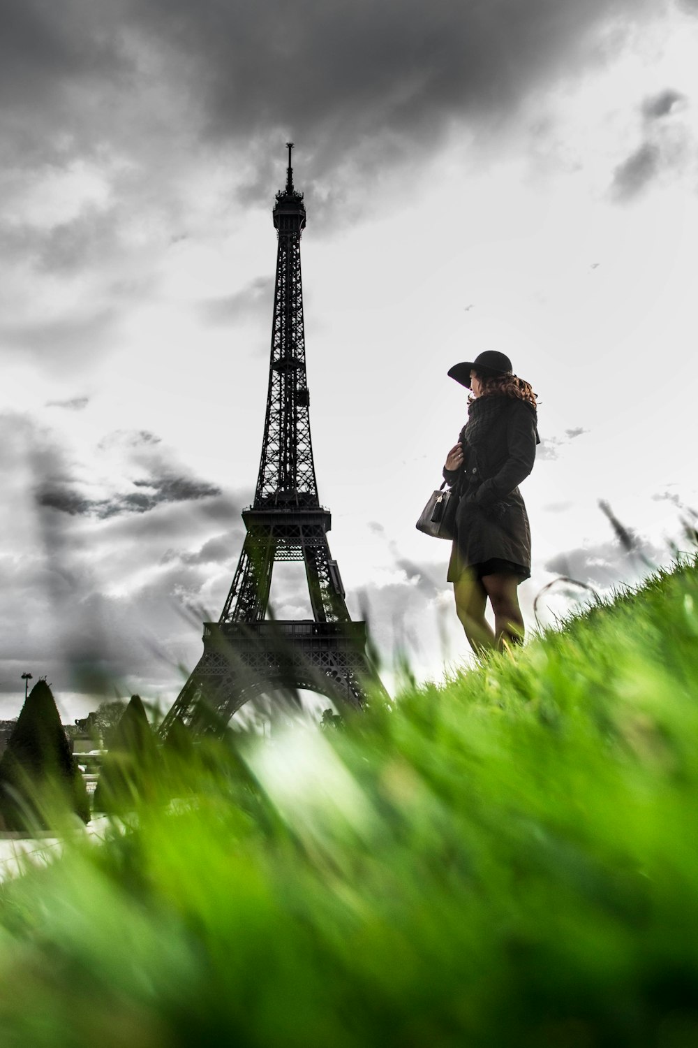 Mann in schwarzer Jacke und schwarzem Hut sitzt tagsüber auf grünem Gras in der Nähe des Eiffelturms