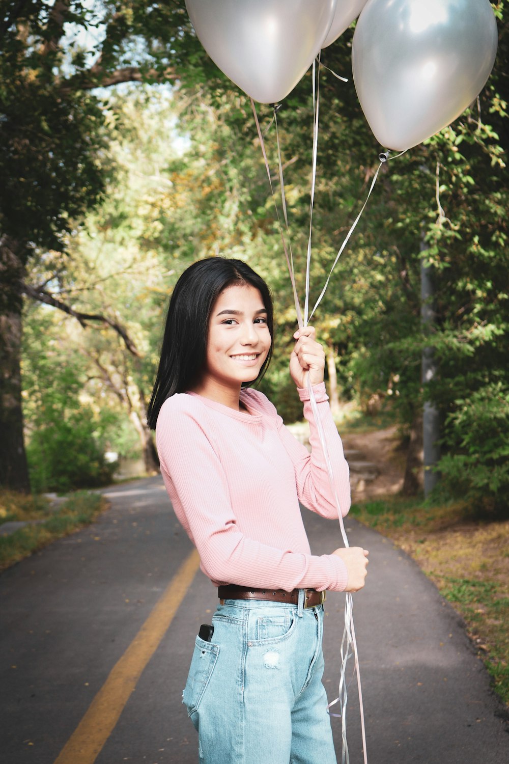 woman in pink long sleeve shirt and blue denim jeans holding white balloons