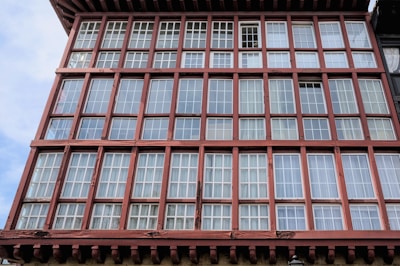 A facade of a building featuring multiple rows of large panes of glass framed in wooden grids. The structure has a reddish-brown wooden framework that creates a geometric pattern.