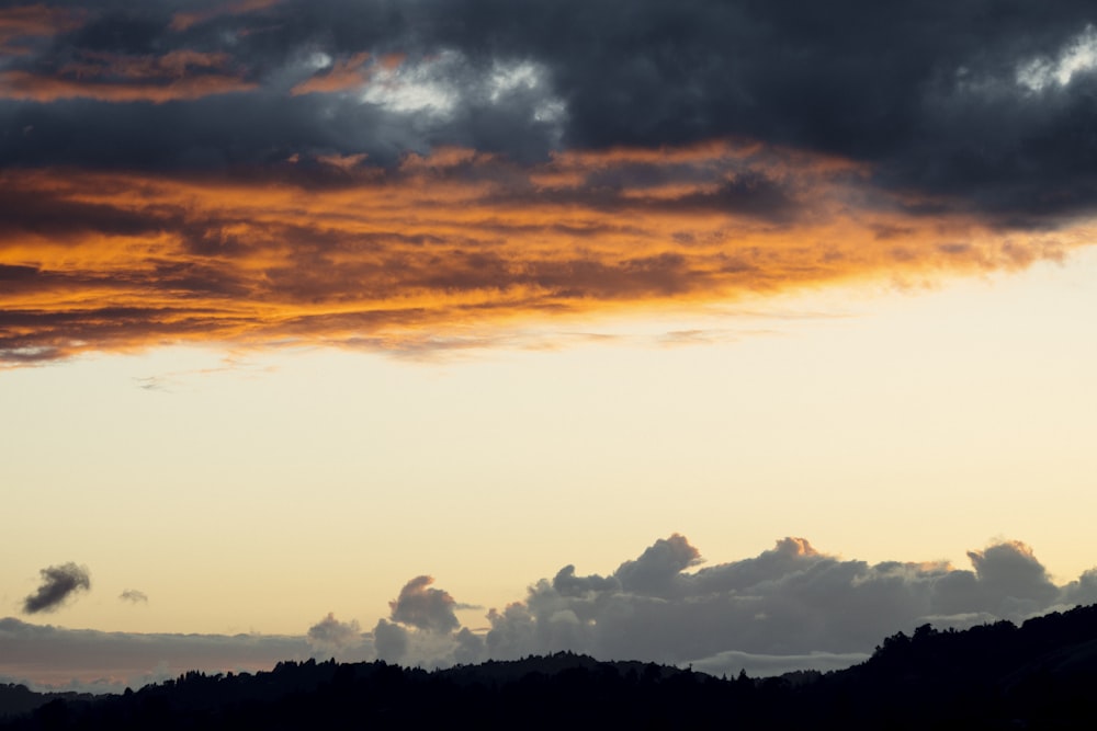 silhouette of mountains under cloudy sky during sunset