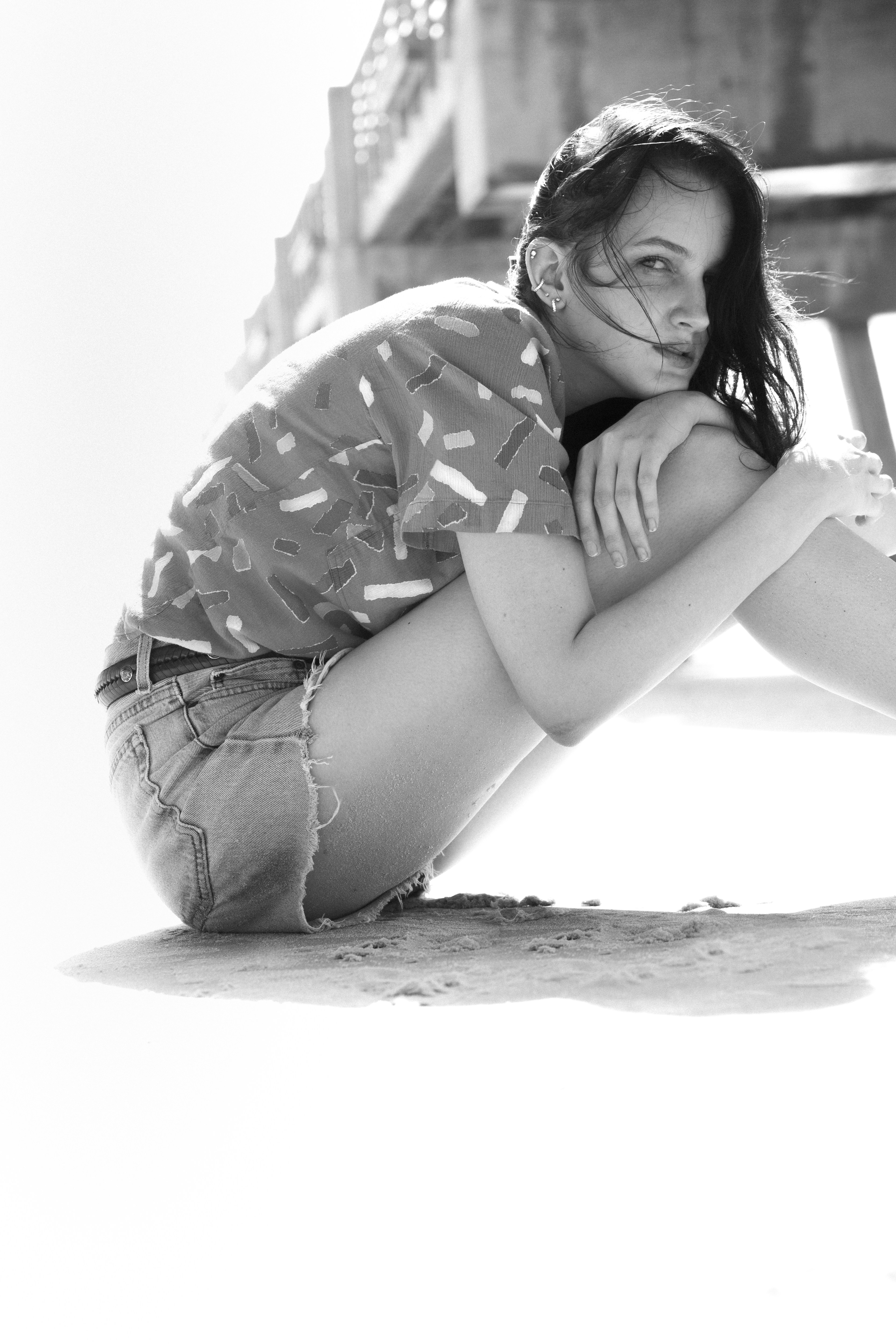 woman in black and white floral shirt and blue denim shorts sitting on sand