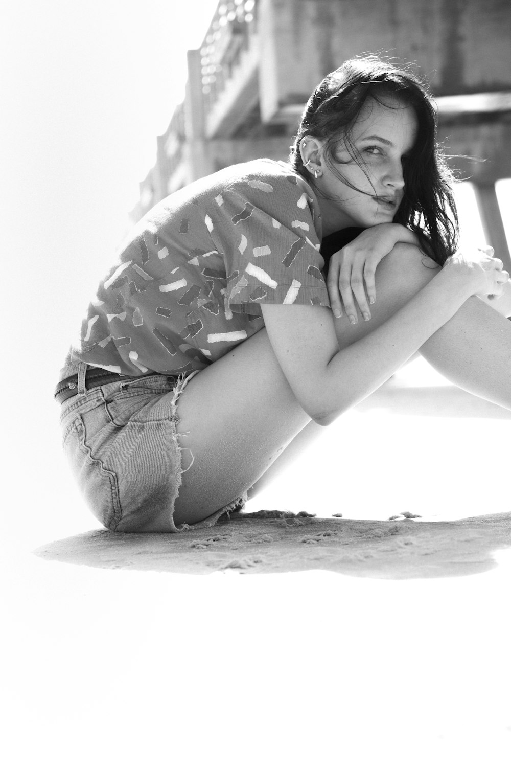 woman in black and white floral shirt and blue denim shorts sitting on sand