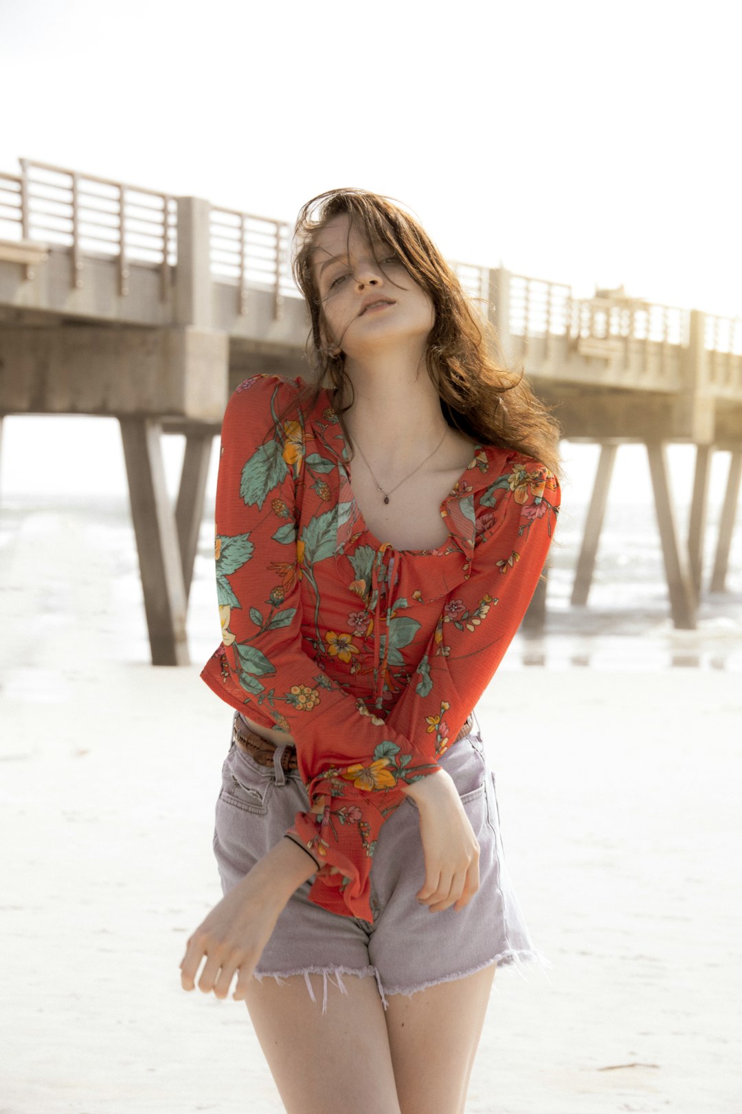 woman in red and blue floral button up shirt and white pants standing on white sand