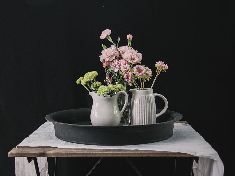 Jarrón de cerámica blanca con flores rosas sobre mesa de madera marrón