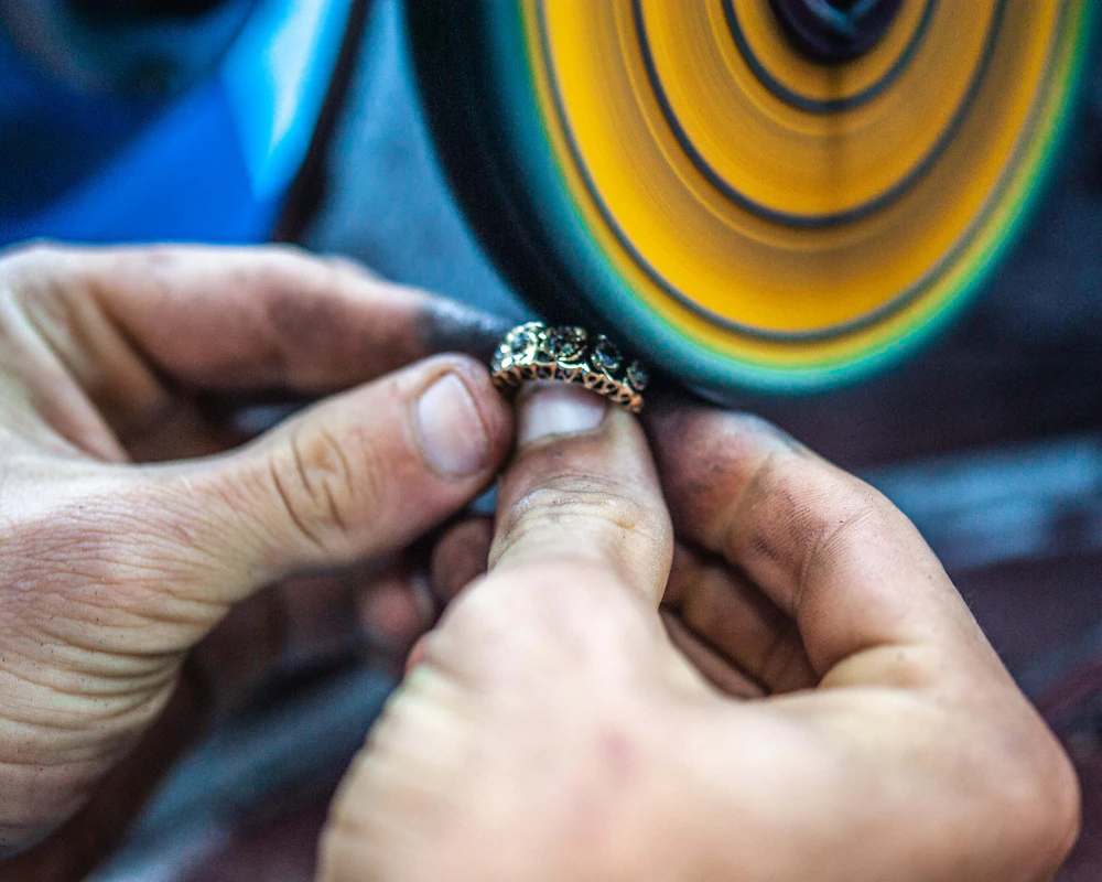 Hands polishing a ring against a spinning polishing wheel