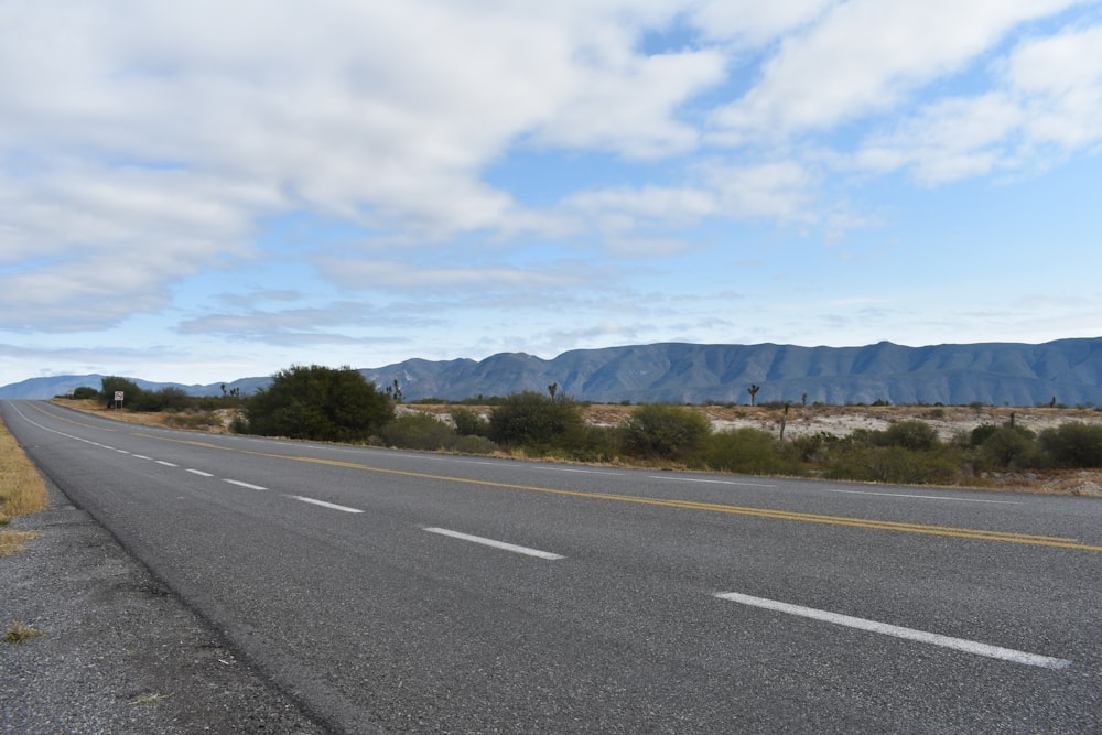 gray asphalt road near green trees and mountains during daytime