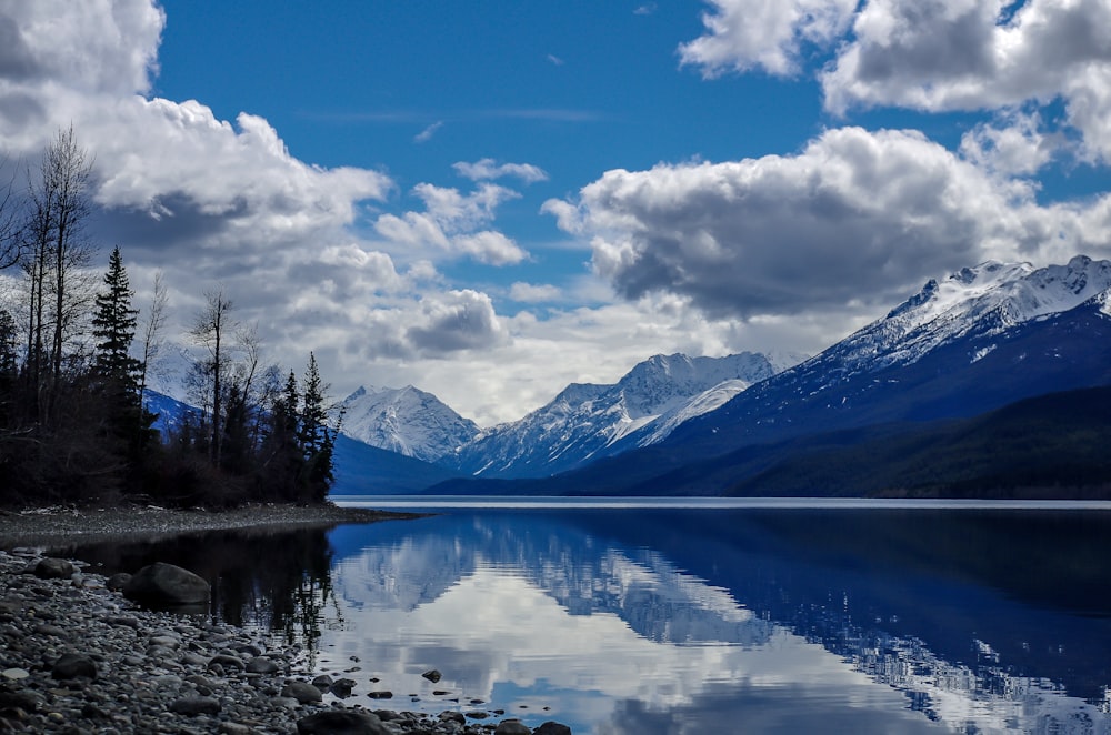 lake near mountain under blue sky and white clouds during daytime